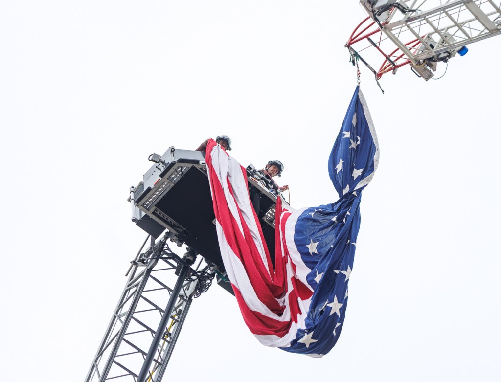 Santa Cruz firefighters lower a large American flag suspended between two ladders during the annual 9/11 Memorial Stair Climb at Seacliff State Beach in Aptos.